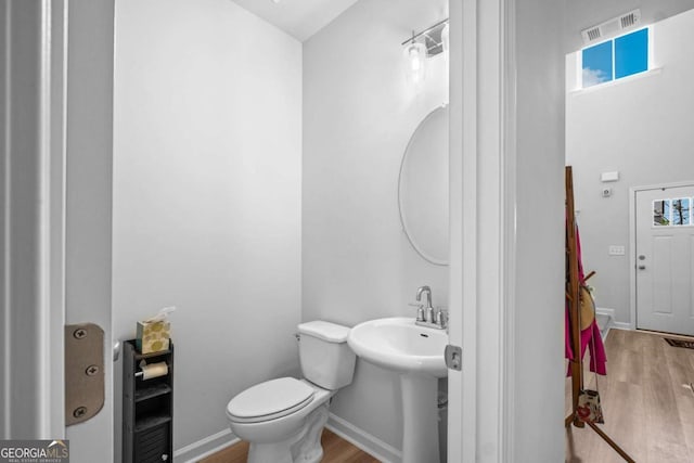 half bath featuring toilet, visible vents, a wealth of natural light, and wood finished floors