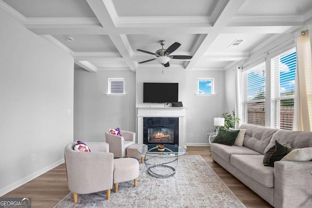living area featuring a glass covered fireplace, wood finished floors, beamed ceiling, baseboards, and a ceiling fan