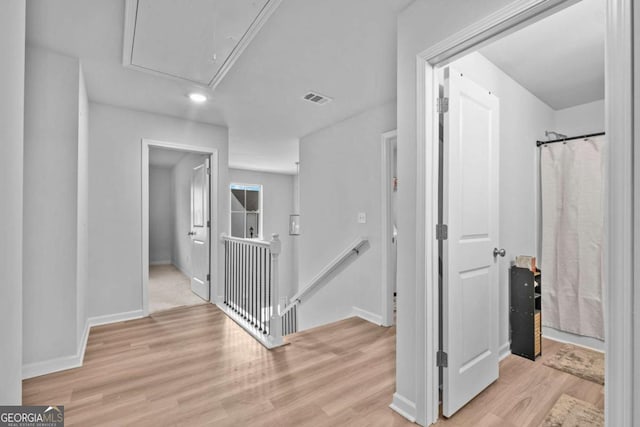 hall with attic access, visible vents, light wood-type flooring, baseboards, and an upstairs landing