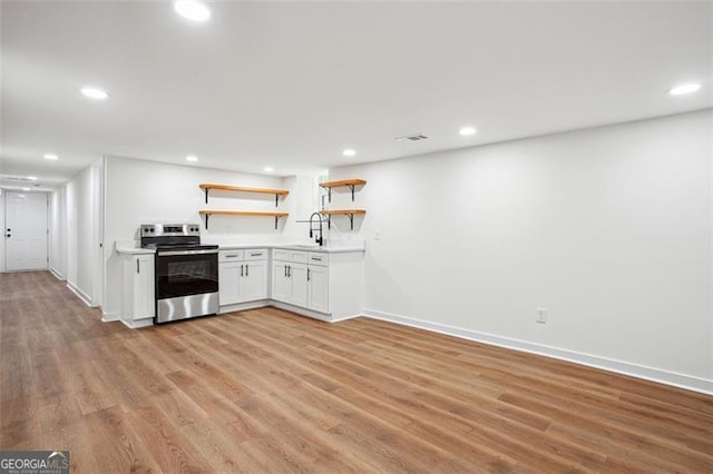kitchen with open shelves, electric range, light countertops, light wood finished floors, and a sink
