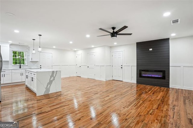 unfurnished living room featuring visible vents, a decorative wall, and light wood-style floors