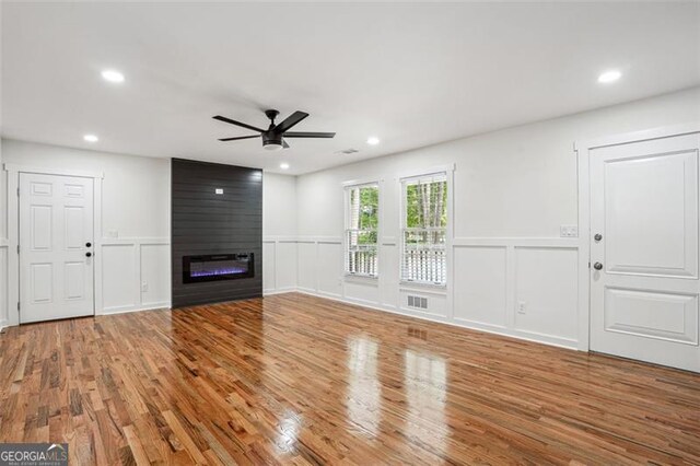 unfurnished living room with wood finished floors, ceiling fan, and a decorative wall