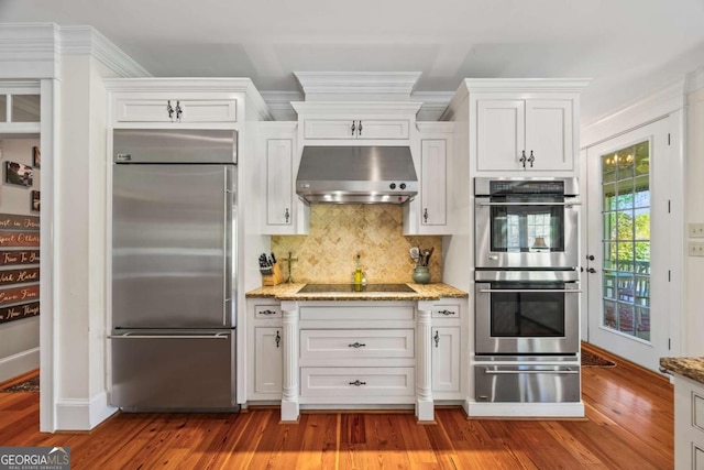 kitchen with range hood, light stone countertops, stainless steel appliances, tasteful backsplash, and a warming drawer