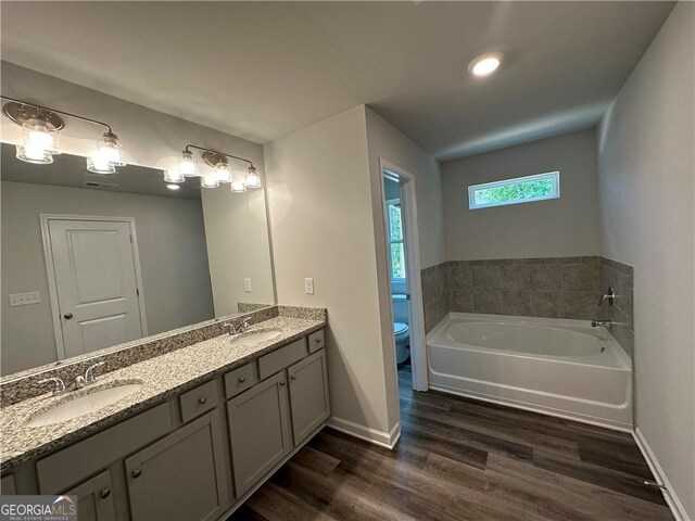 full bath with a sink, a bath, wood finished floors, and toilet