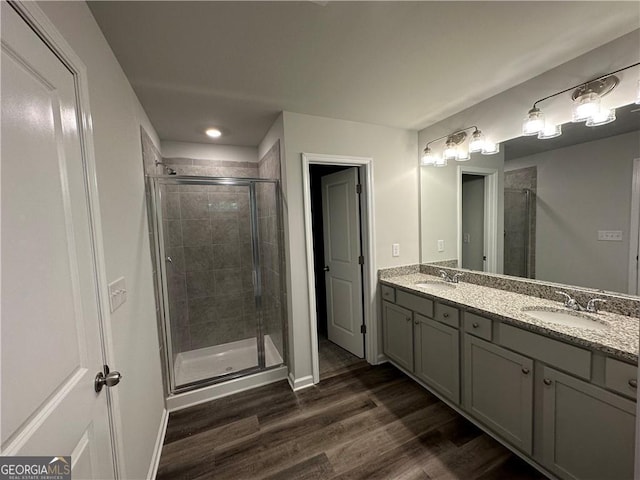 full bath with double vanity, a sink, wood finished floors, and a shower stall