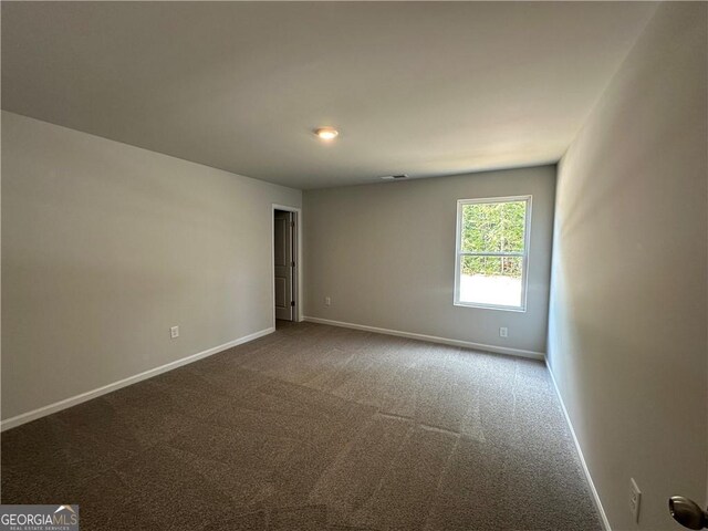 unfurnished room with baseboards and dark carpet