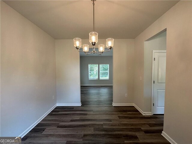 unfurnished dining area with baseboards, an inviting chandelier, and dark wood-type flooring