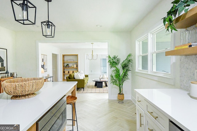 interior space featuring light countertops, white cabinetry, stainless steel microwave, open floor plan, and decorative light fixtures