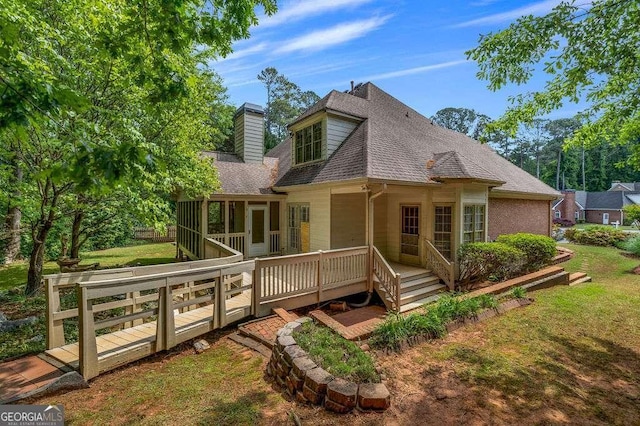 back of house featuring a lawn, a wooden deck, a chimney, and roof with shingles