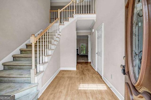 entryway with crown molding, stairs, baseboards, wood finished floors, and a high ceiling