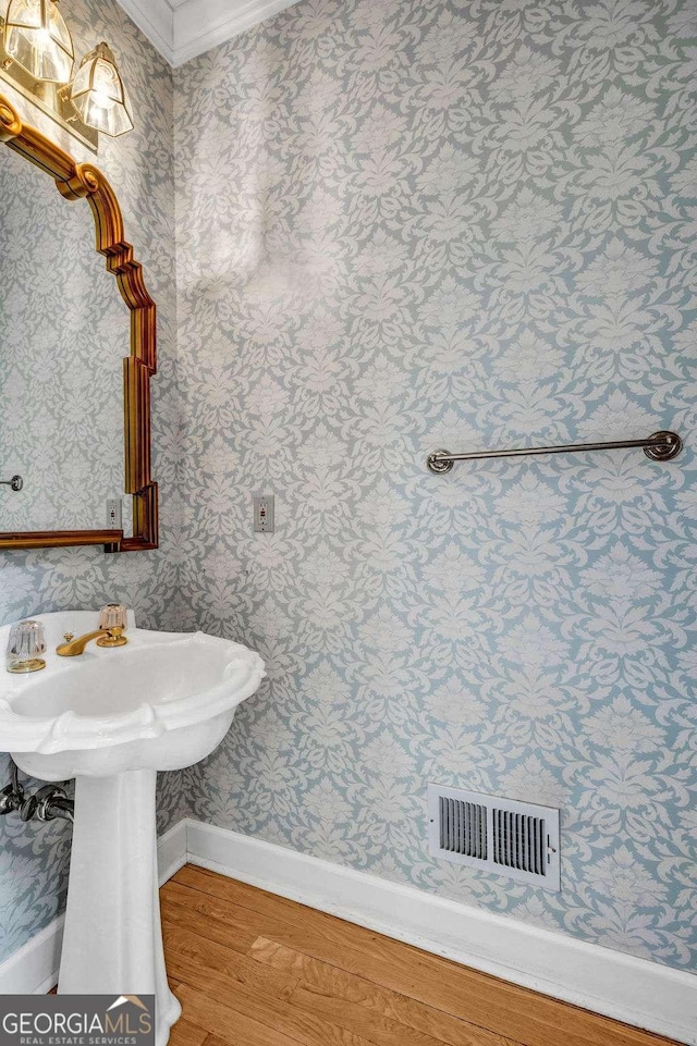 bathroom featuring visible vents, baseboards, ornamental molding, wallpapered walls, and wood finished floors