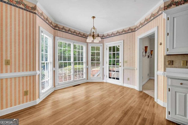 unfurnished dining area with ornamental molding, a chandelier, light wood-style flooring, and wallpapered walls