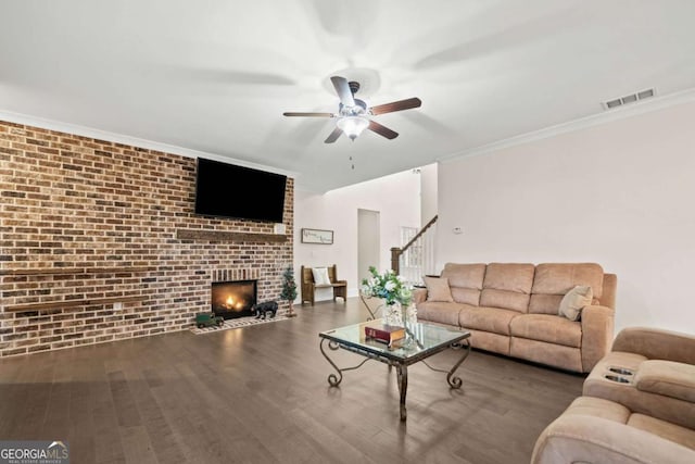 living area with ceiling fan, brick wall, visible vents, a brick fireplace, and stairs