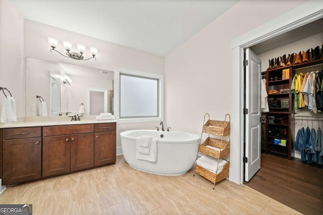 bathroom with a freestanding tub, a spacious closet, wood finished floors, and vanity