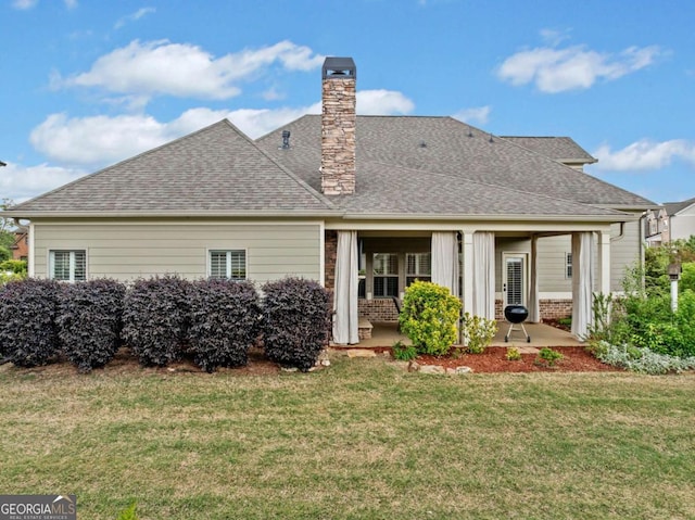 rear view of house featuring a lawn, a patio, a chimney, and a shingled roof