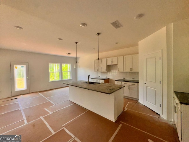 7252 Eton Ln, Locust Grove, GA 30248 - kitchen with visible vents, dark countertops, a center island with sink, a sink, and white cabinets