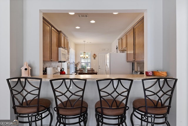 145 Begonia Ct, Griffin, GA 30223 - kitchen featuring white appliances, brown cabinets, decorative backsplash, a peninsula, and recessed lighting