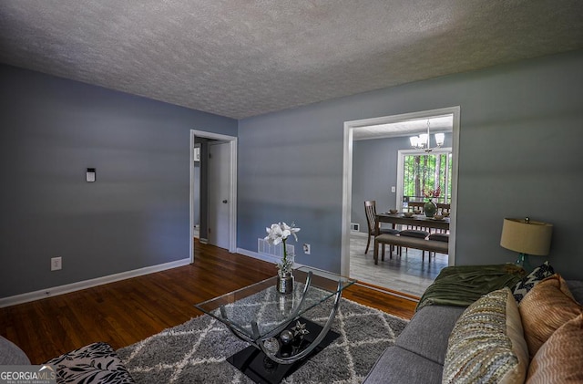 living room featuring wood finished floors, a chandelier, baseboards, and a textured ceiling