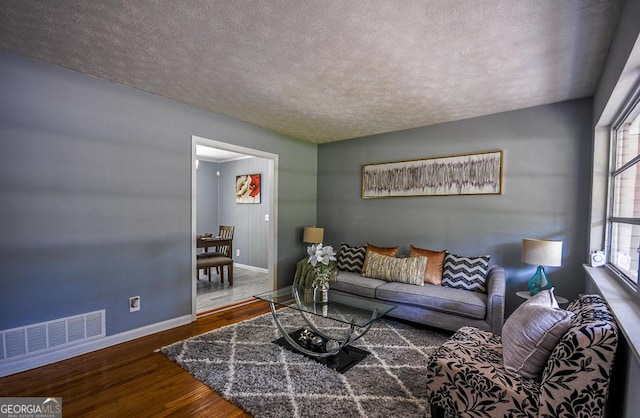 living area with a textured ceiling, visible vents, wood finished floors, and baseboards