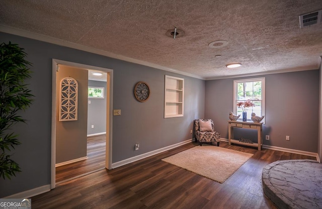sitting room with dark wood-type flooring, baseboards, visible vents, a textured ceiling, and crown molding
