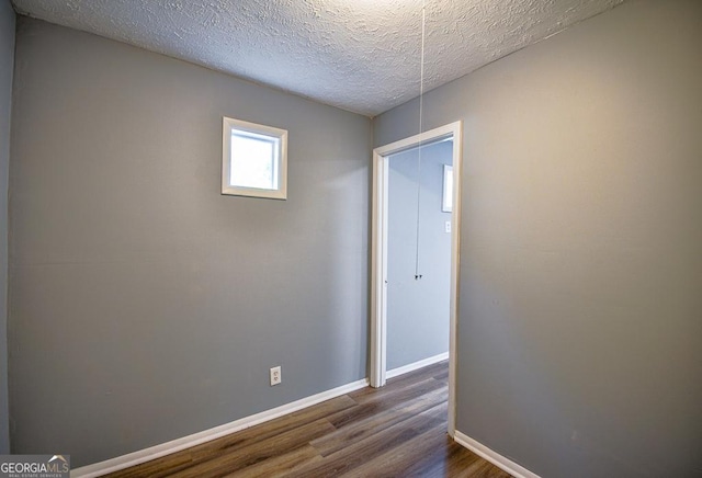 unfurnished room featuring a textured ceiling, dark wood-style floors, and baseboards