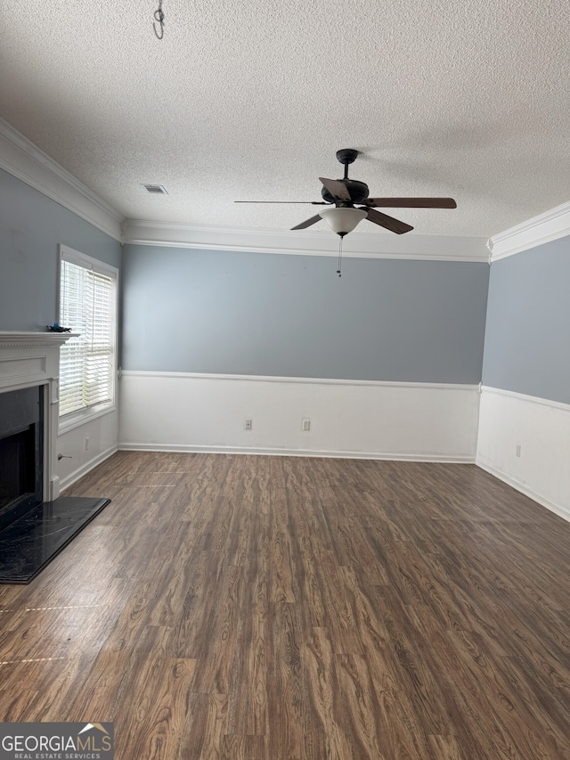 unfurnished living room featuring wood finished floors, a textured ceiling, a fireplace with raised hearth, crown molding, and a ceiling fan