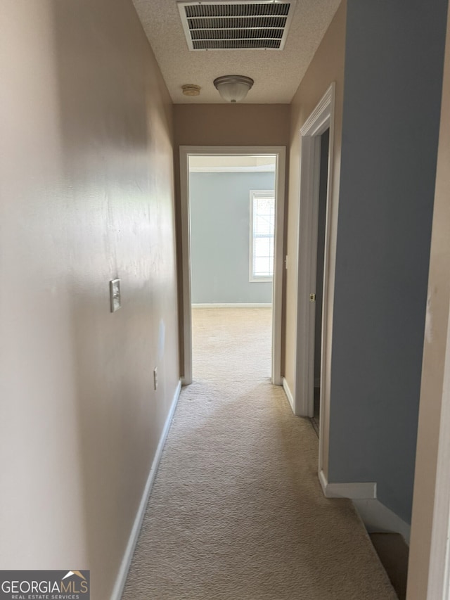 hallway with a textured ceiling, carpet, baseboards, and visible vents