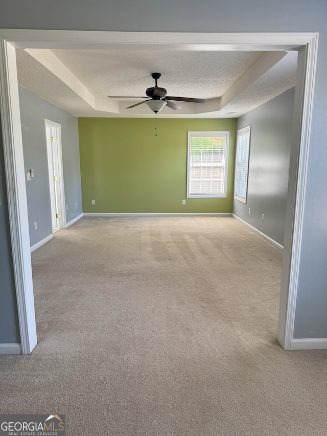 carpeted empty room featuring baseboards, a raised ceiling, ceiling fan, and a textured ceiling