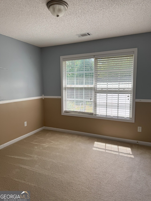 carpeted spare room with baseboards, visible vents, and a textured ceiling