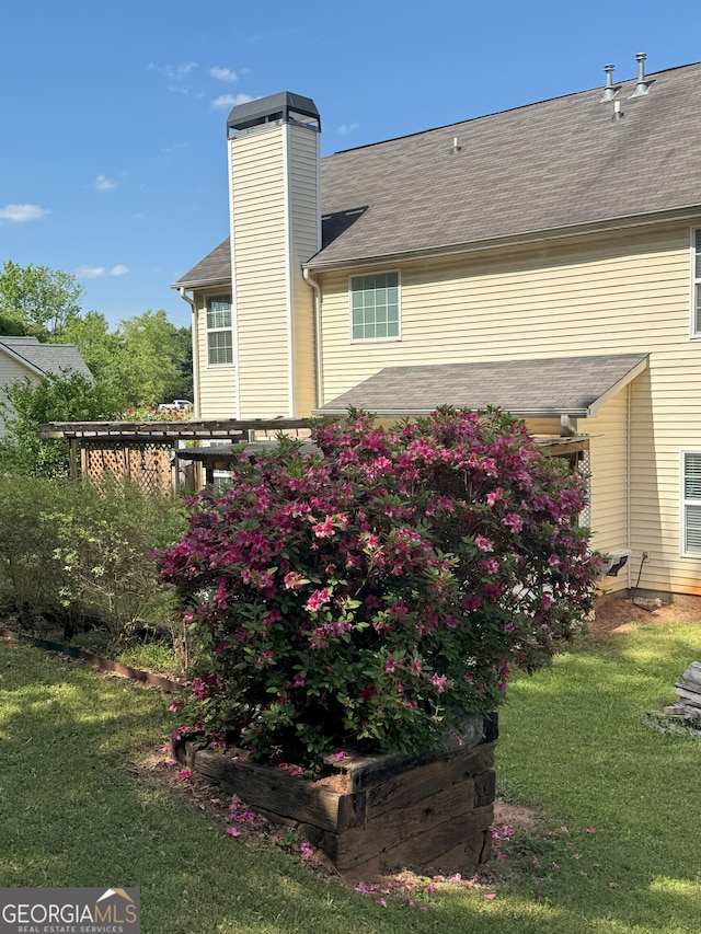 back of property with roof with shingles, a chimney, and a lawn