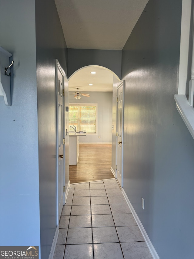 hall with arched walkways, baseboards, and light tile patterned floors