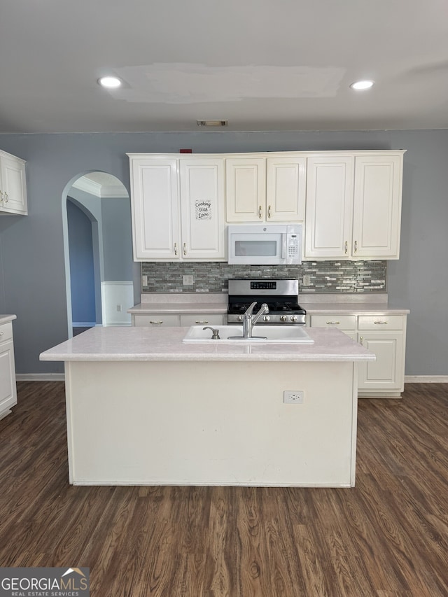 kitchen featuring white microwave, light countertops, arched walkways, and stainless steel gas range