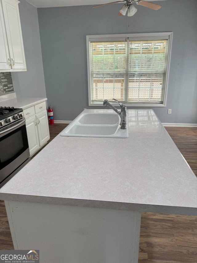kitchen featuring stainless steel gas range, a sink, white cabinets, ceiling fan, and dark wood-style floors