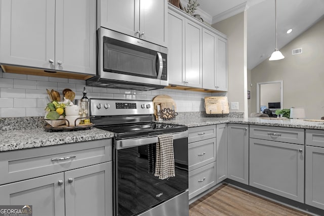 kitchen with tasteful backsplash, light stone counters, appliances with stainless steel finishes, ornamental molding, and light wood finished floors