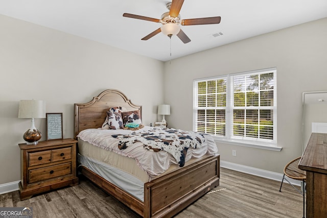 bedroom featuring wood finished floors, a ceiling fan, visible vents, and baseboards