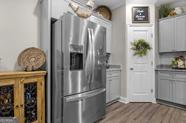 kitchen with tasteful backsplash, crown molding, stainless steel refrigerator with ice dispenser, gray cabinetry, and wood finished floors