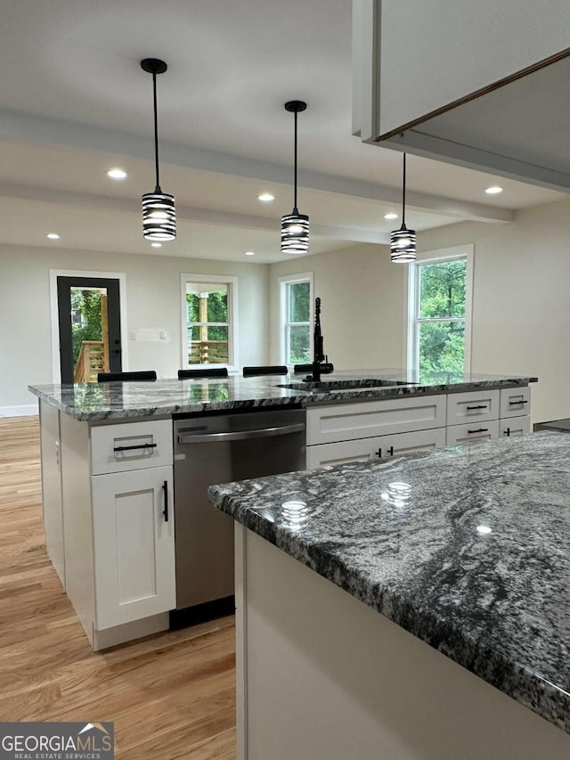 kitchen featuring pendant lighting, white cabinetry, stainless steel dishwasher, a sink, and light wood finished floors