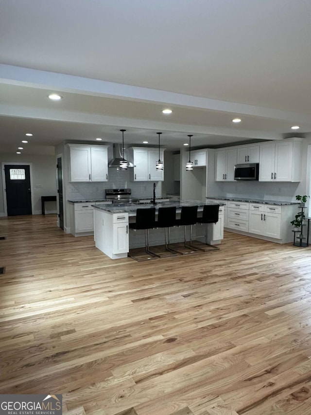 kitchen with wall chimney range hood, stainless steel appliances, light wood finished floors, and white cabinets