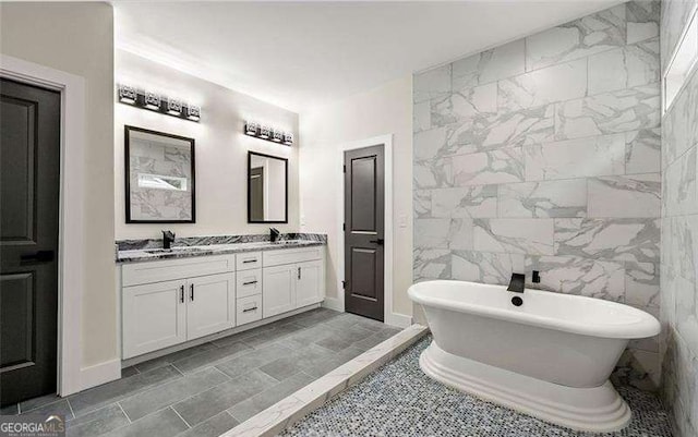 bathroom with double vanity, tile walls, a freestanding bath, and a sink