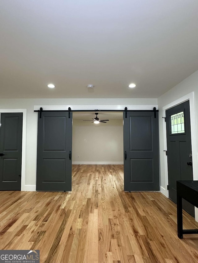 basement with baseboards, a barn door, light wood finished floors, and recessed lighting