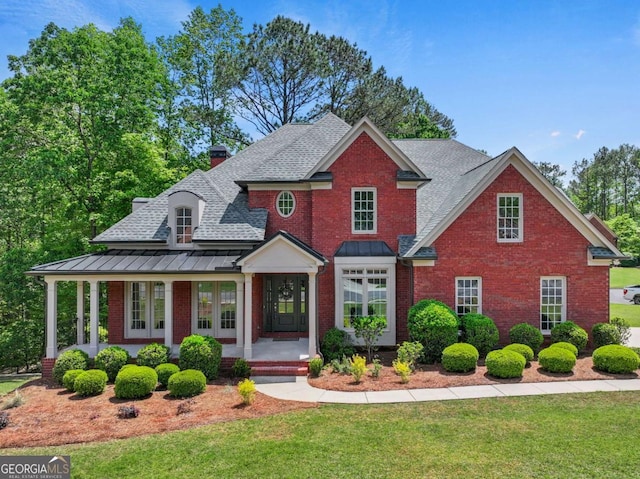 view of front facade featuring a standing seam roof, a front yard, a shingled roof, and brick siding