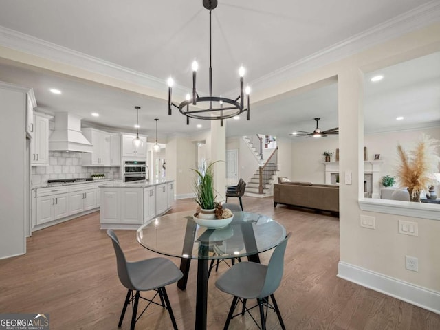 dining space featuring ceiling fan with notable chandelier, crown molding, light wood-style flooring, and baseboards