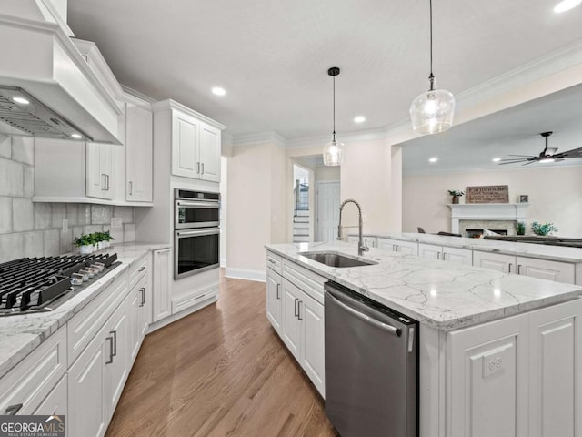 kitchen with a kitchen island with sink, custom range hood, appliances with stainless steel finishes, white cabinets, and a sink