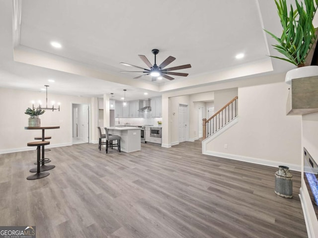 living room featuring recessed lighting, a tray ceiling, light wood-style flooring, baseboards, and ceiling fan with notable chandelier