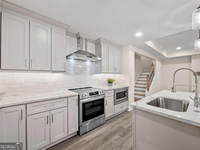 kitchen with light wood-style flooring, decorative backsplash, stainless steel appliances, a sink, and wall chimney exhaust hood