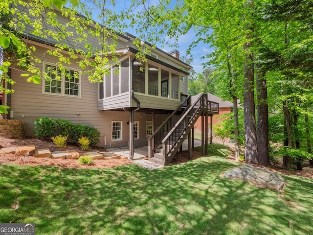rear view of house featuring a chimney, a deck, a yard, a sunroom, and stairs