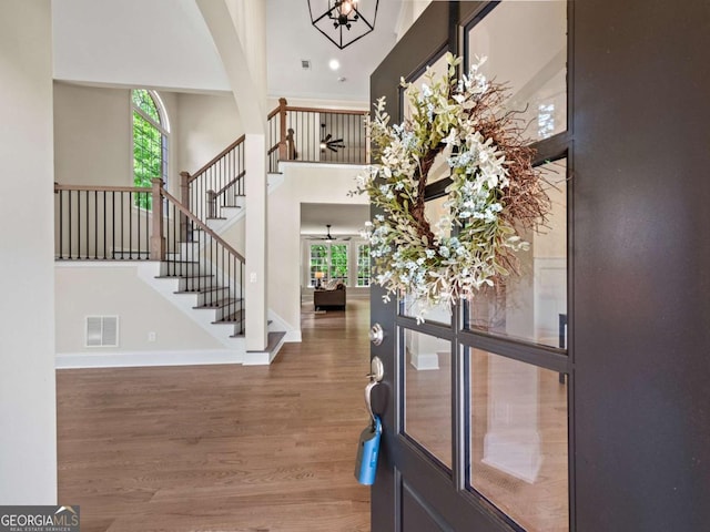 foyer featuring visible vents, an inviting chandelier, a towering ceiling, wood finished floors, and stairs
