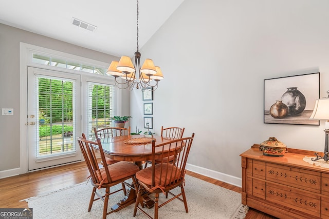 dining space featuring visible vents, wood finished floors, baseboards, a notable chandelier, and lofted ceiling