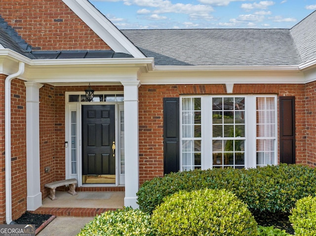 property entrance featuring brick siding and a shingled roof