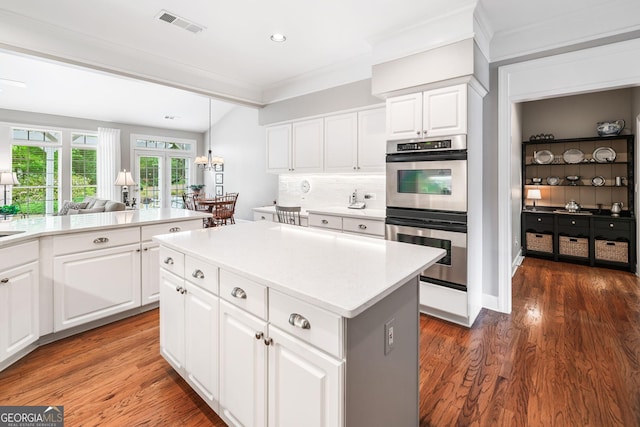 kitchen with visible vents, ornamental molding, a kitchen island, stainless steel double oven, and light countertops